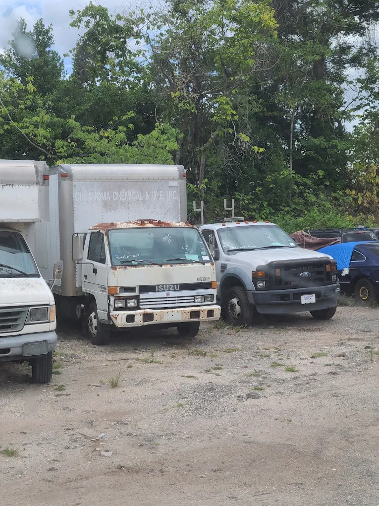 Isuzu box truck and Ford pickup parked at lot with trees behind