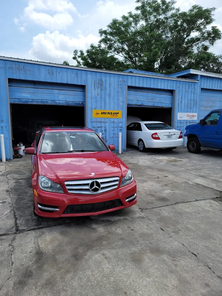 Red Mercedes-Benz parked outside blue automotive repair garage with other vehicles