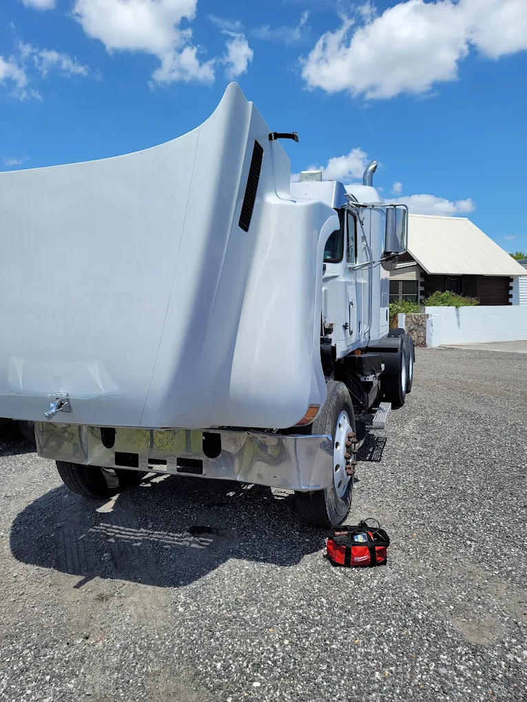 White commercial truck with open cargo box door parked on gravel driveway
