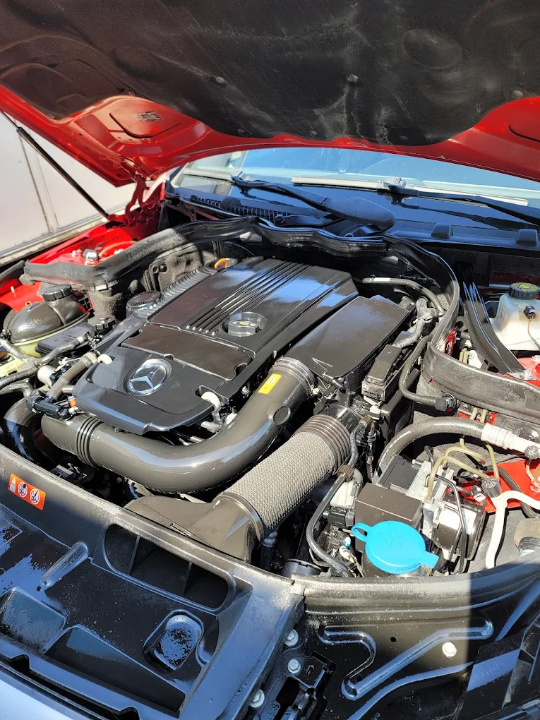 Open engine bay of red Mercedes-Benz showing turbocharged engine with blue coolant reservoir