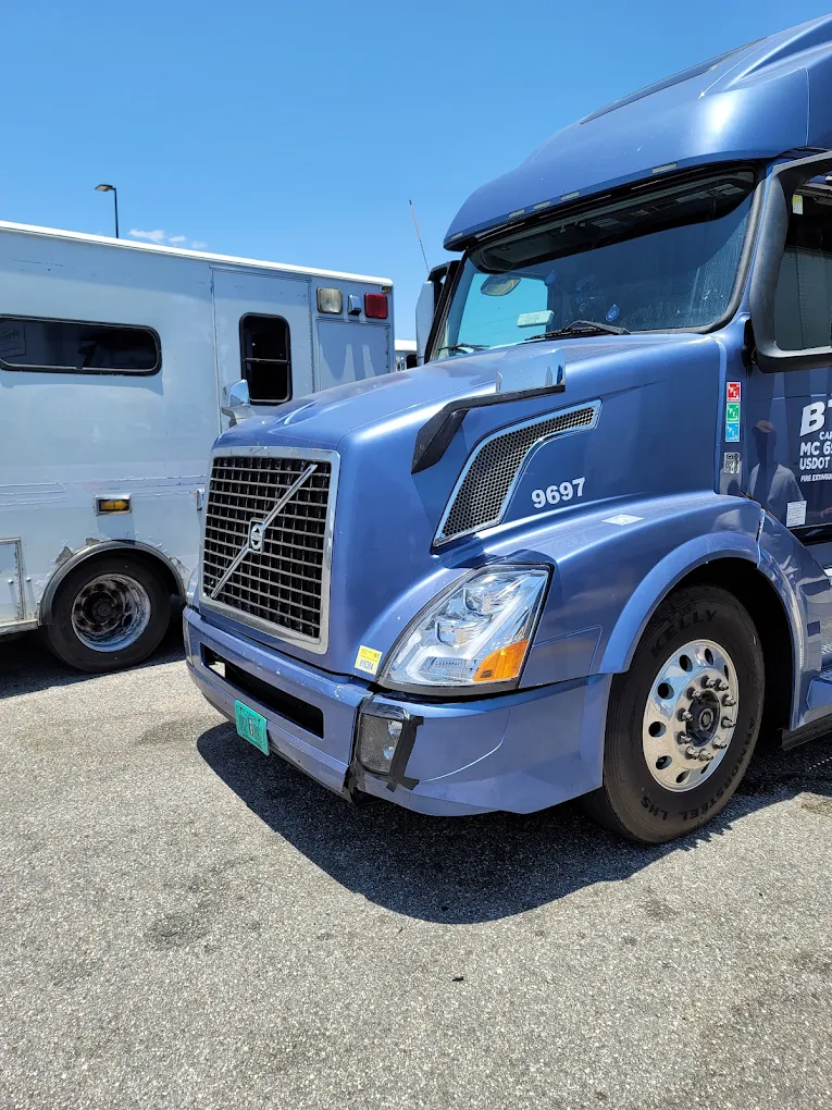 Blue Volvo semi truck numbered 9697 parked next to white trailer in lot