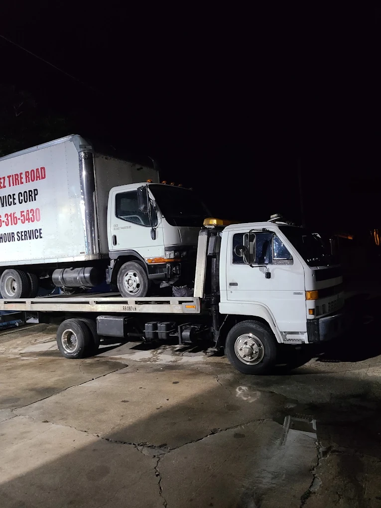 White tow truck carrying another white commercial truck on flatbed at night